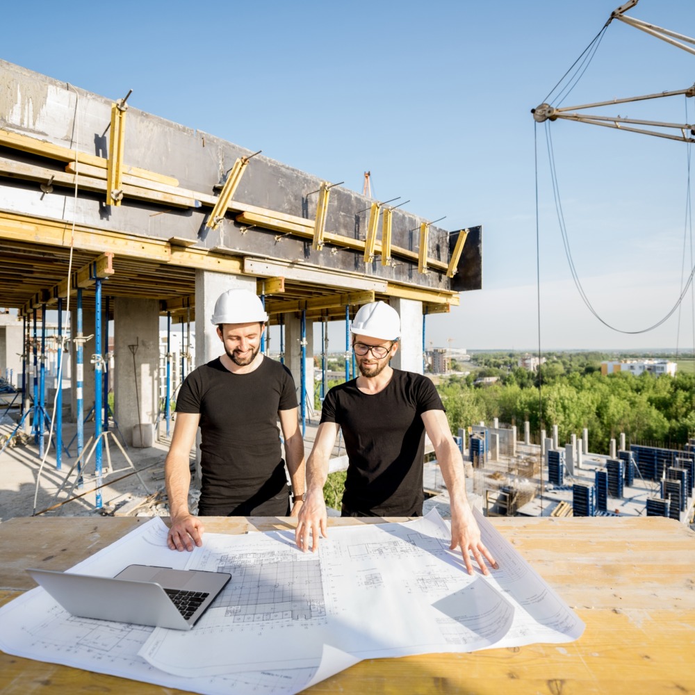 Two workers in black t-shirts and protective harhats working with drawings at the construction site outdoors